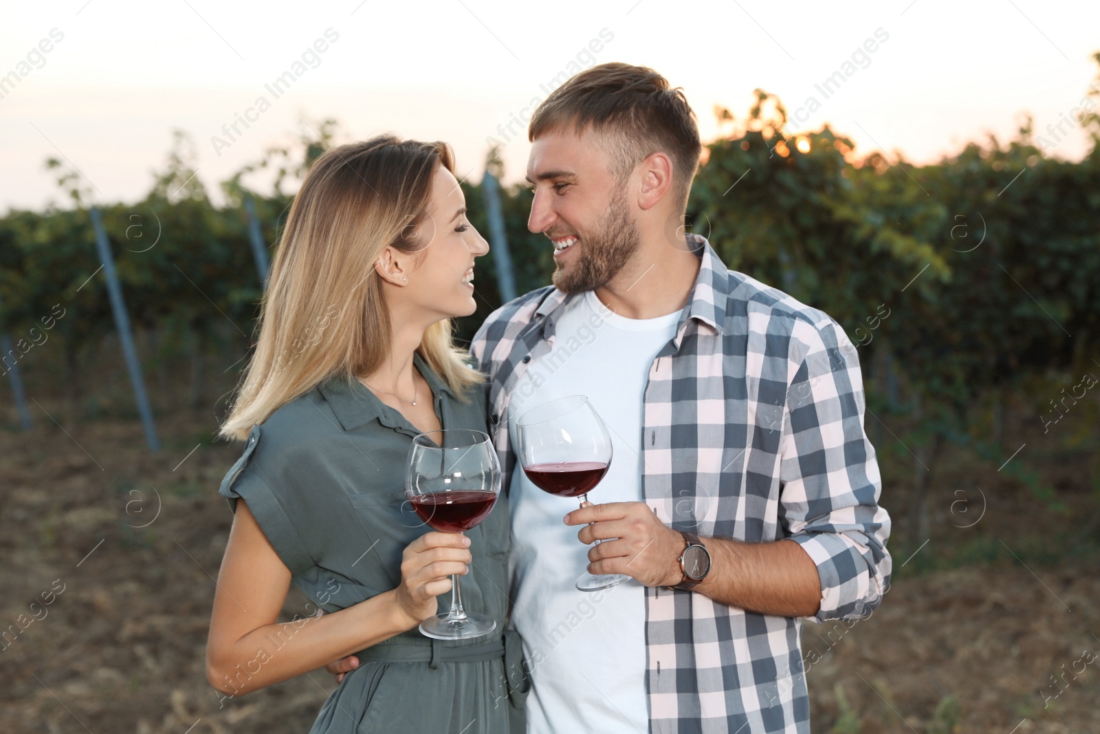 Photo of Young romantic couple holding glasses of wine at vineyard