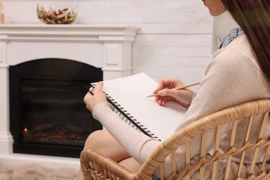 Photo of Young woman drawing in sketchbook at home, closeup. Space for text