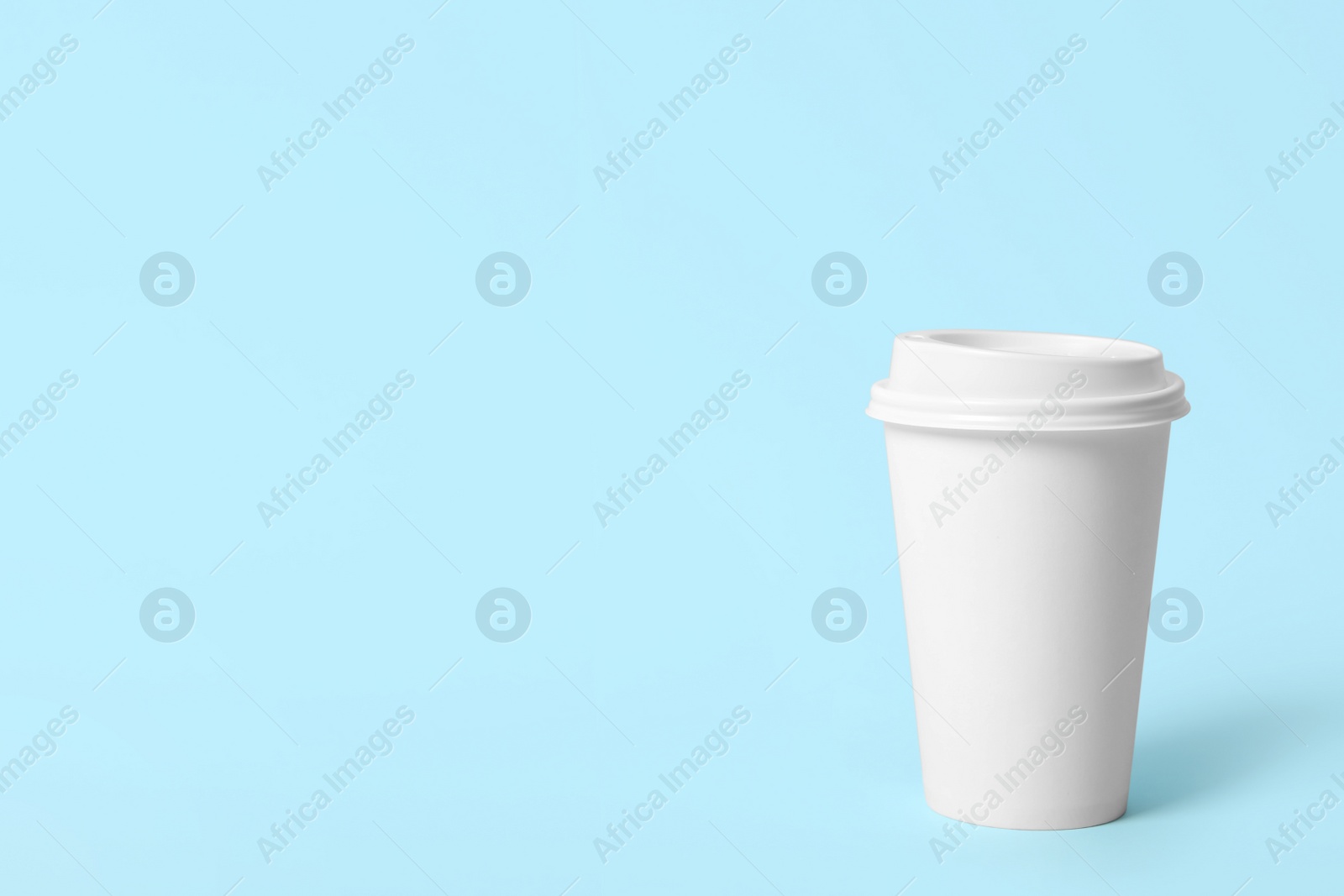 Photo of Takeaway paper coffee cup on light blue background. Space for text