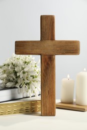 Photo of Burning church candles, wooden cross, ecclesiastical books and flowers on white table