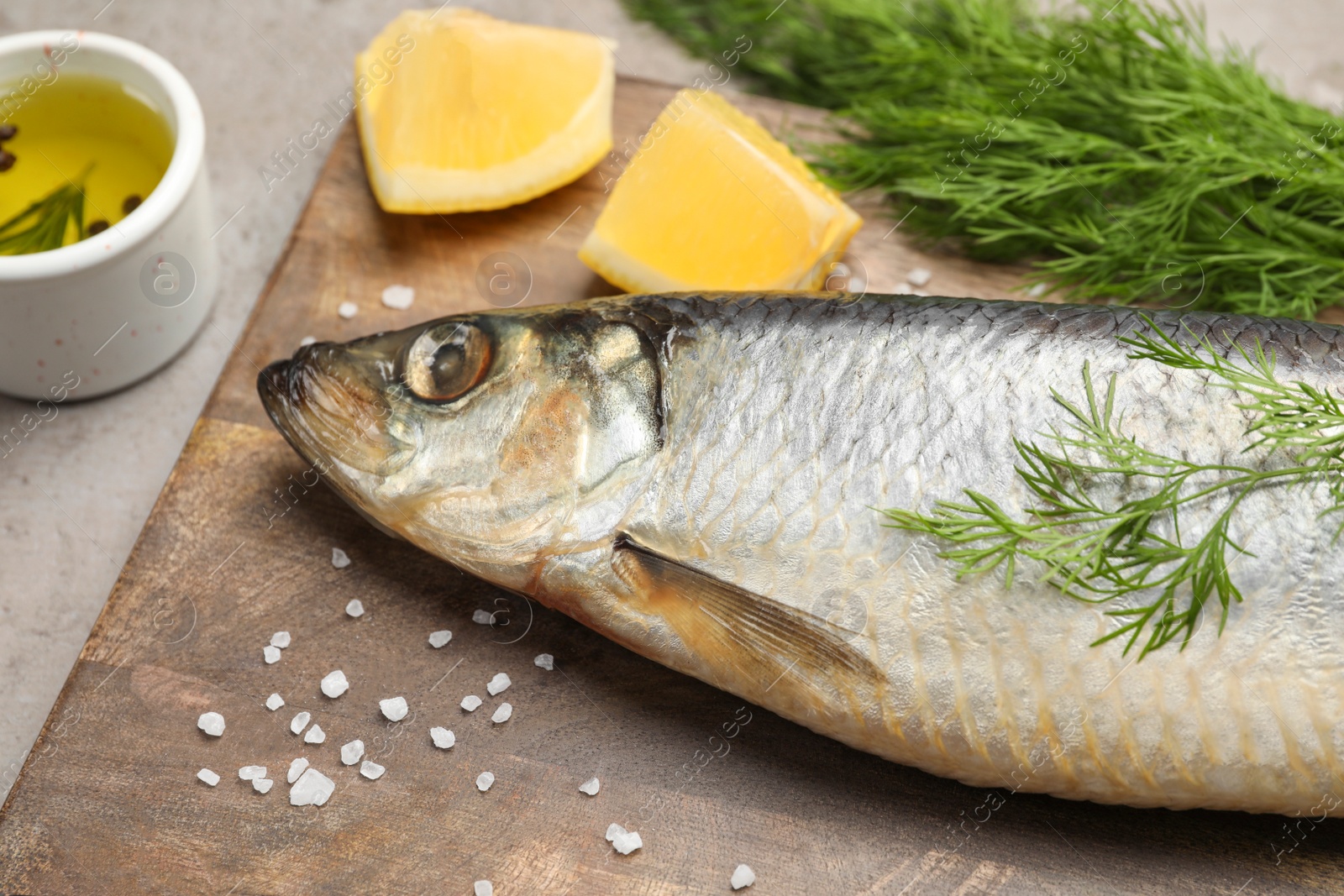 Photo of Board with delicious salted herring, dill, lemon and olive oil on grey table, closeup