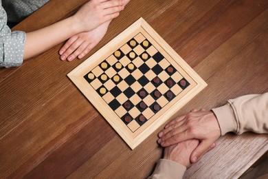 Photo of Man playing checkers with woman at wooden table, above view