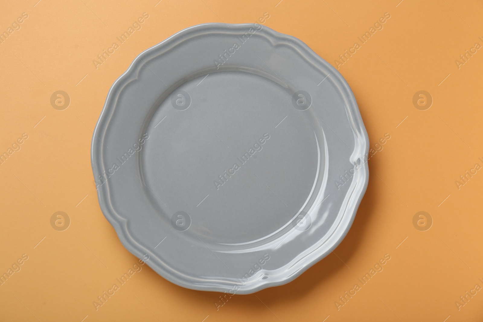 Photo of Empty ceramic plate on pale orange background, top view