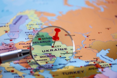 Photo of Looking at pinned Ukraine on map of Europe through magnifier, closeup. International relationships