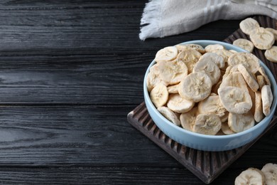 Photo of Bowl and dried banana slices on black wooden table. Space for text
