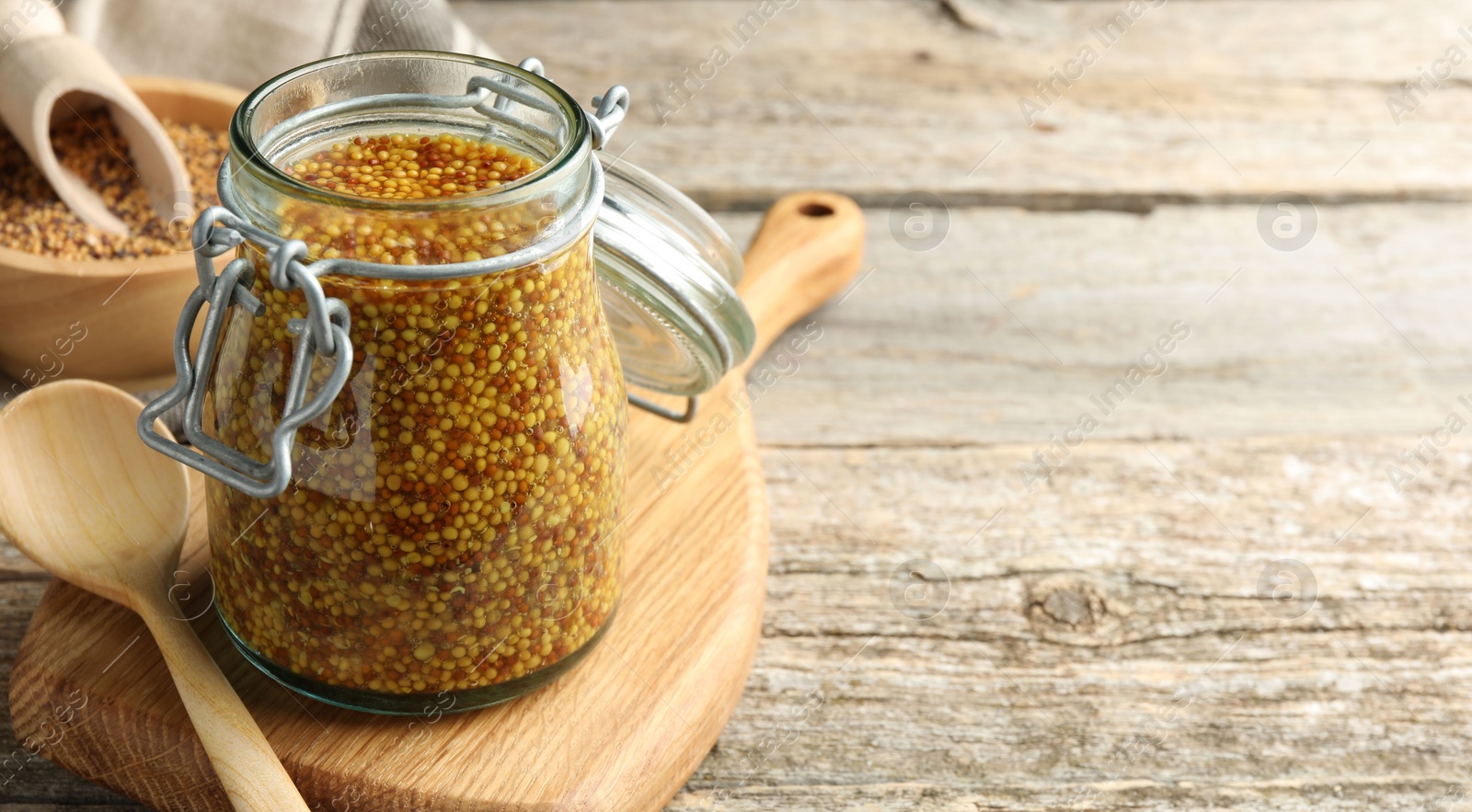 Photo of Whole grain mustard in jar and spoon on wooden table. Space for text