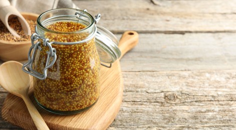 Photo of Whole grain mustard in jar and spoon on wooden table. Space for text