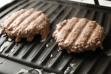 Delicious hamburger patties cooking on electric grill, closeup