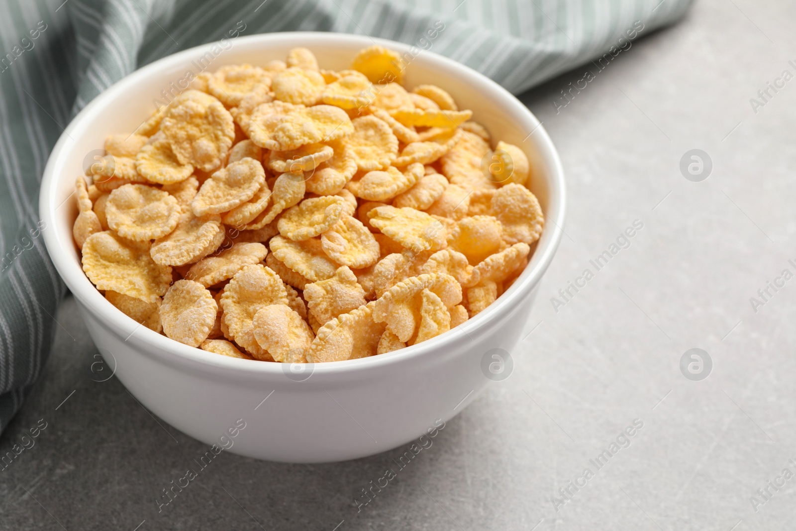 Photo of Bowl of tasty corn flakes on light grey background, closeup. Space for text