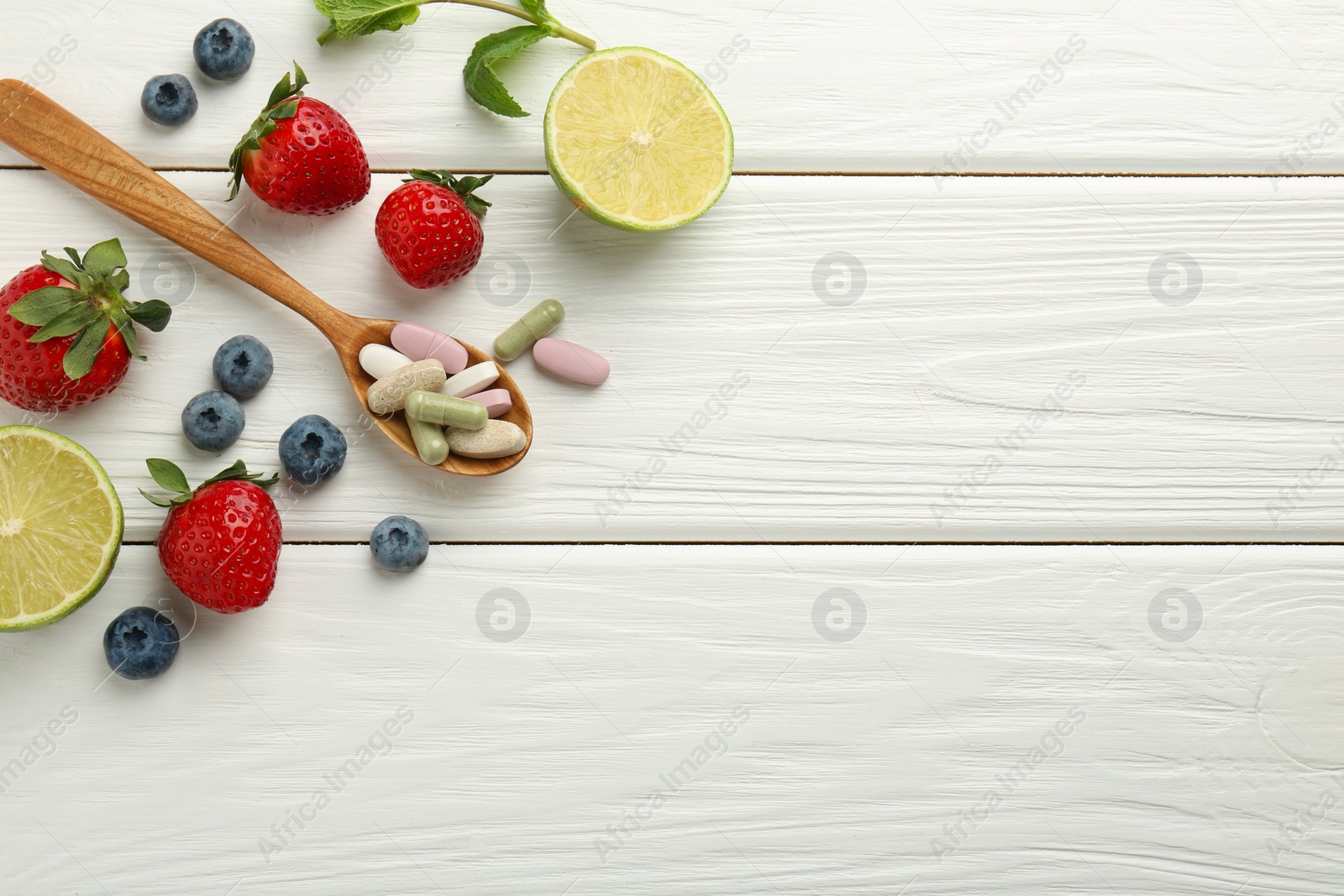 Photo of Different vitamin pills in spoon and fresh fruits on white wooden table, flat lay. Space for text