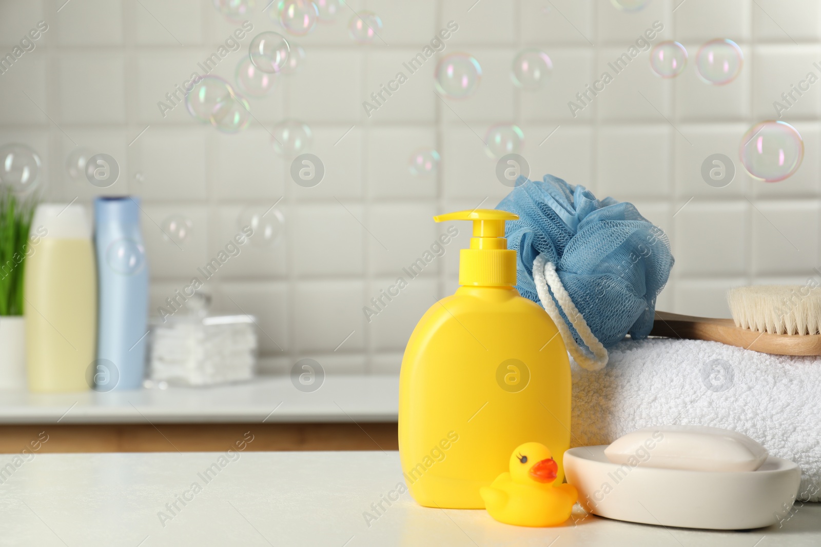 Photo of Baby cosmetic products, bath duck, brush and towel on white table against soap bubbles. Space for text