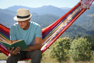 Photo of Handsome man reading book in hammock outdoors on sunny day