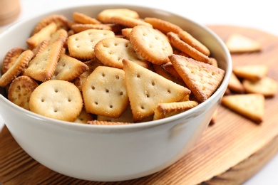 Photo of Delicious crispy crackers in bowl on wooden board, closeup