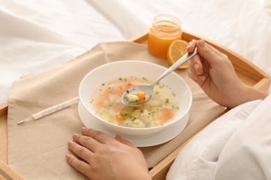 Sick woman eating fresh homemade soup to cure flu in bed at home, closeup