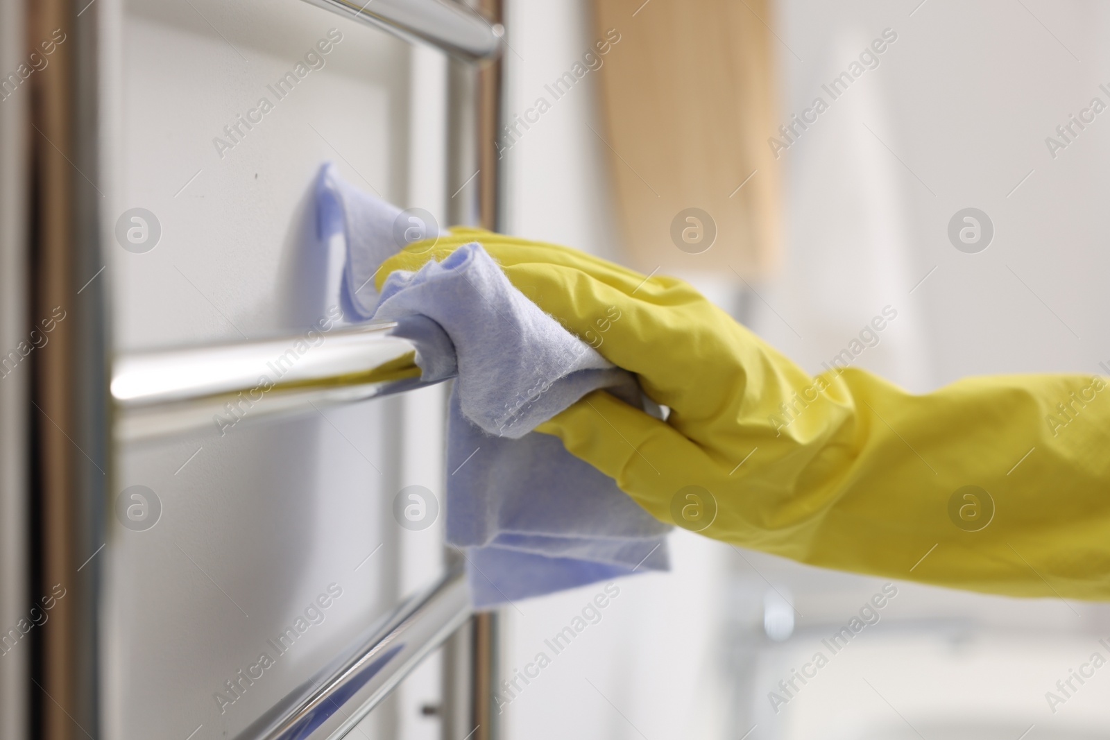 Photo of Woman cleaning heated towel rail with rag indoors, closeup