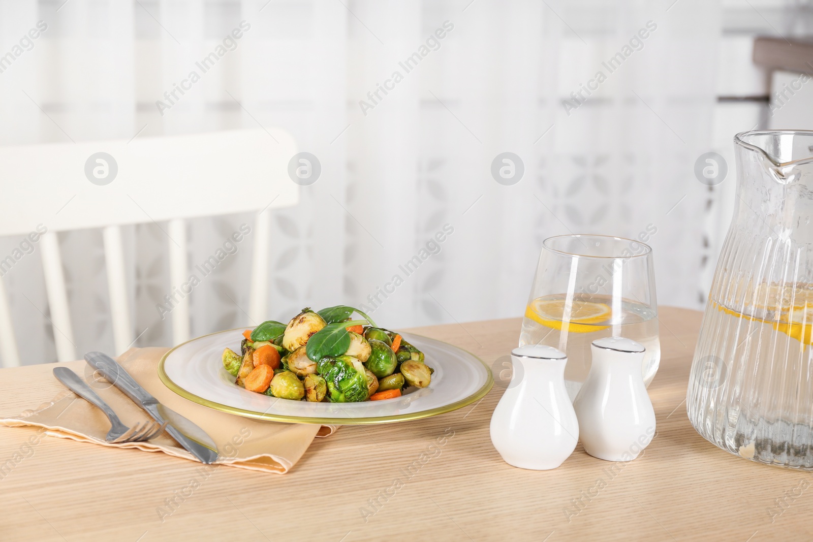 Photo of Delicious roasted Brussels sprouts and water with lemon served on wooden table indoors