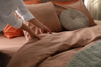 Woman making bed with stylish linens in room, closeup