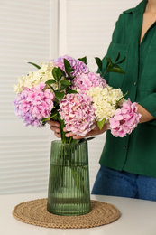 Woman with beautiful hydrangea flowers at table indoors, closeup. Interior design element