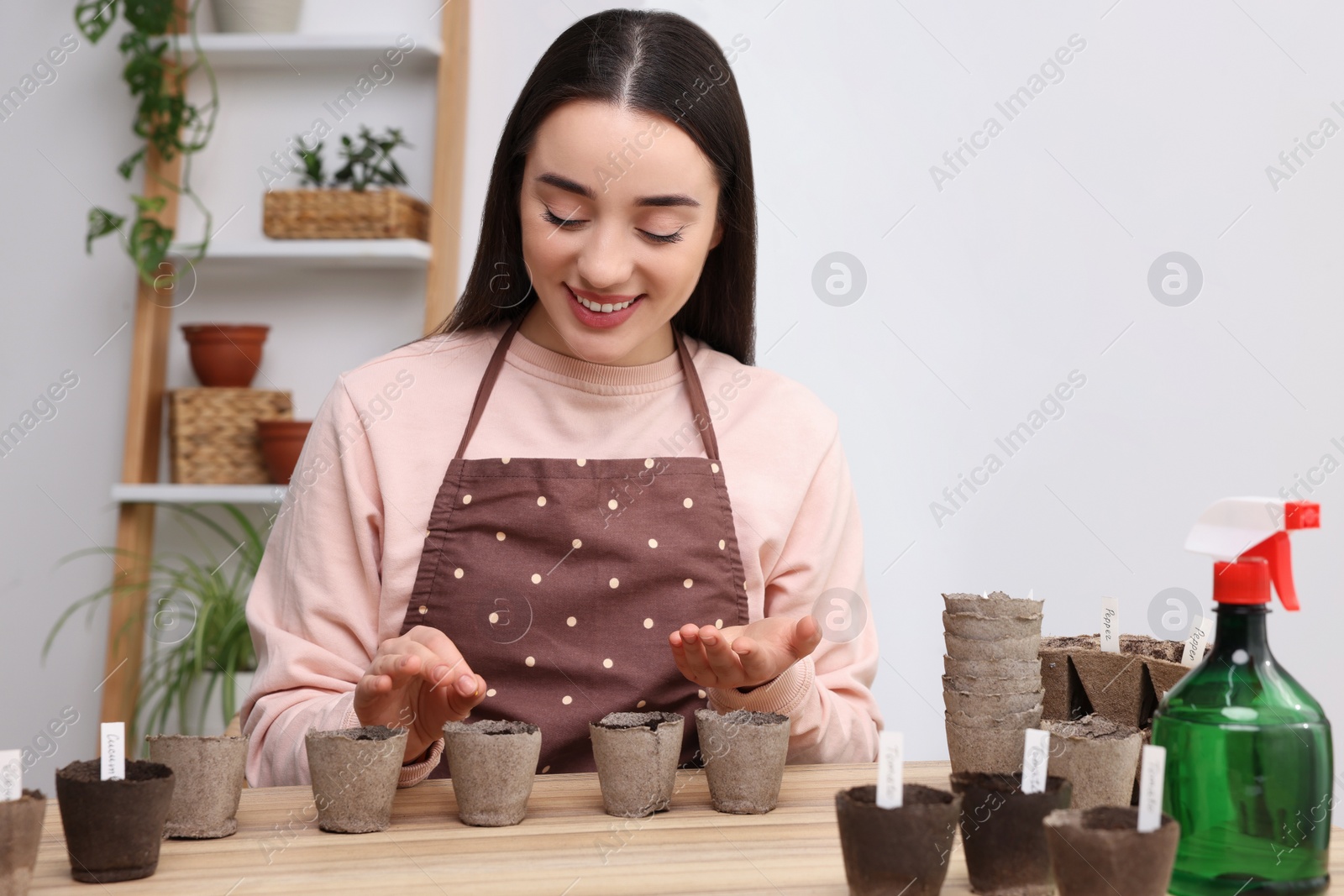 Photo of Woman planting vegetable seeds into peat pots with soil at wooden table indoors