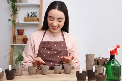 Photo of Woman planting vegetable seeds into peat pots with soil at wooden table indoors