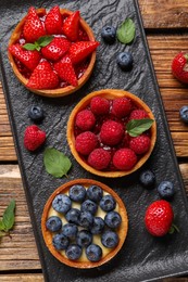 Photo of Tartlets with different fresh berries on wooden table, flat lay. Delicious dessert