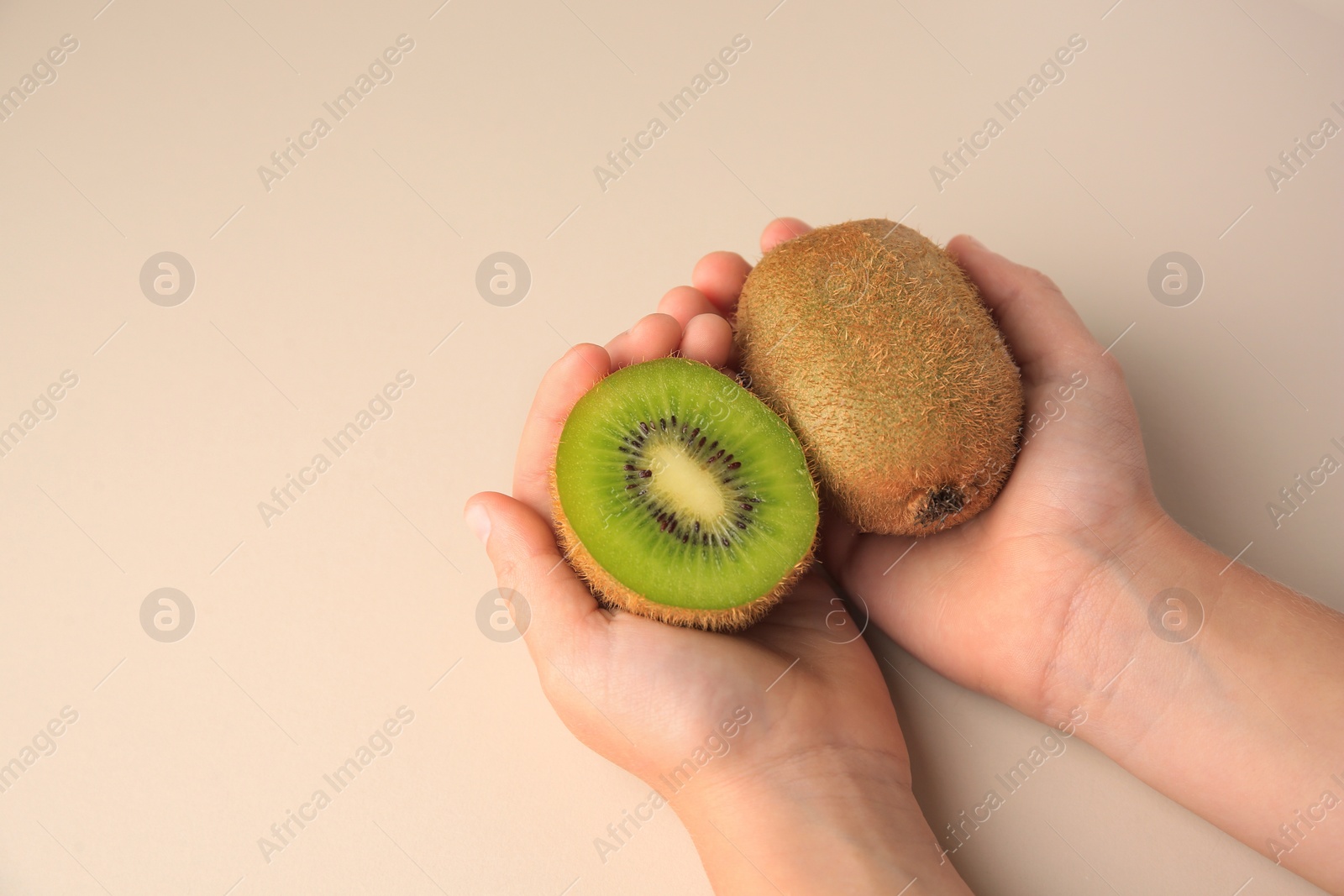 Photo of Woman holding cut and whole fresh kiwis on beige background, top view. Space for text