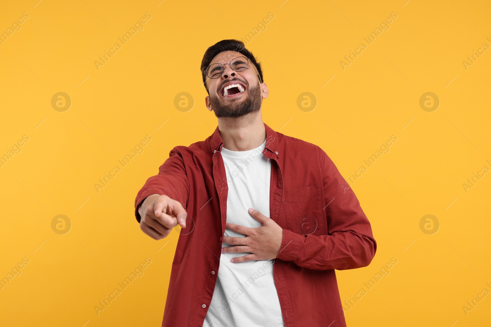 Photo of Handsome young man laughing while pointing at something on yellow background