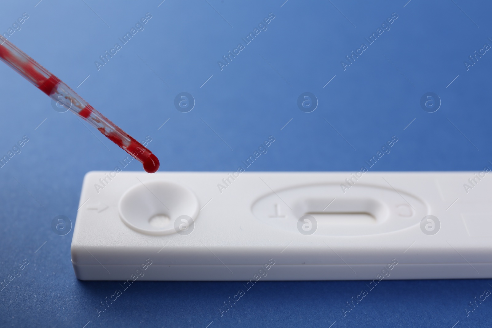 Photo of Dropping blood sample onto disposable express test cassette with pipette on blue background, closeup