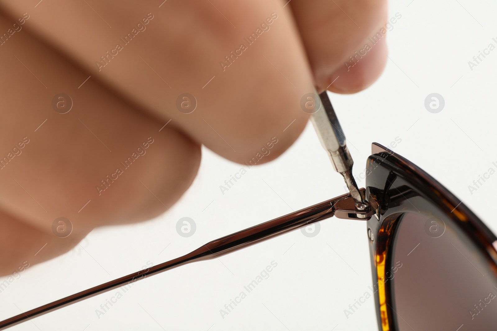 Photo of Handyman repairing sunglasses with screwdriver on white background, closeup