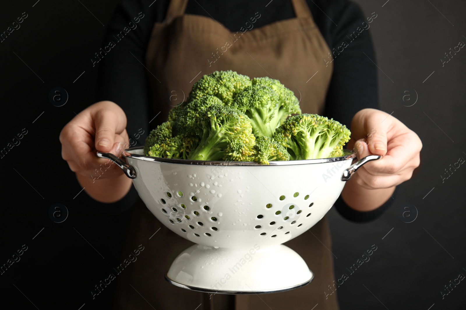 Photo of Woman holding colander with fresh green broccoli on black background, closeup