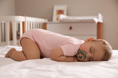 Adorable little baby with pacifier sleeping on bed at home