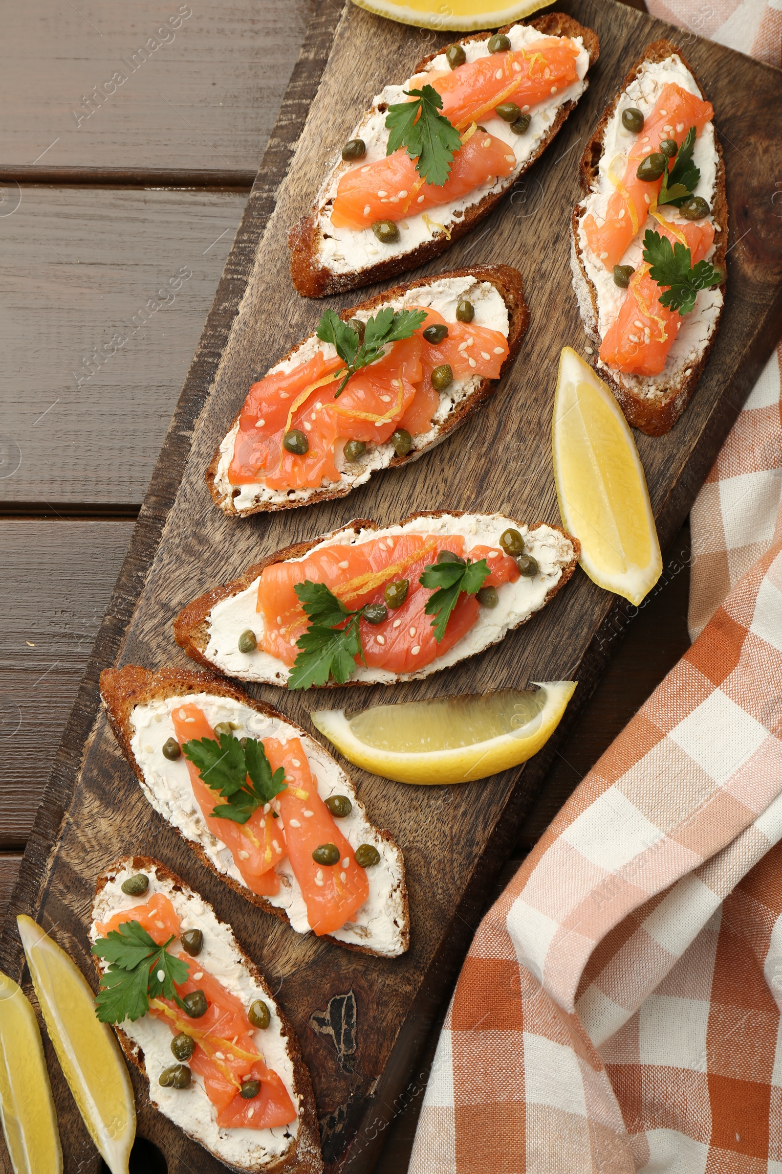 Photo of Tasty canapes with salmon, capers, lemon and cream cheese on wooden table, top view