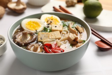 Photo of Noodle soup. Bowl of delicious ramen, ingredients and chopsticks on white tiled table, closeup