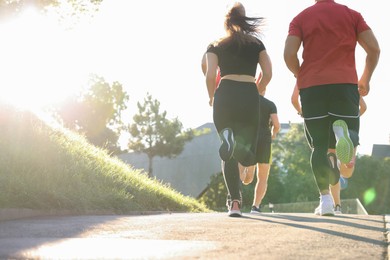 Photo of Group of people running outdoors on sunny day, back view. Space for text