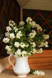Photo of Bouquet of beautiful jasmine flowers in vase on wooden table indoors
