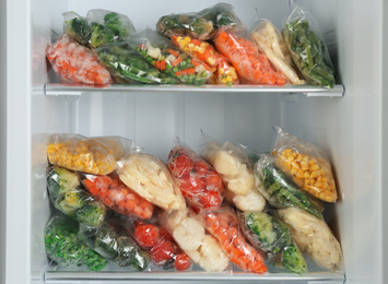 Plastic bags with different frozen vegetables in refrigerator