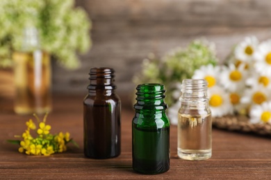 Photo of Bottles of essential oils with flowers on wooden table, space for text