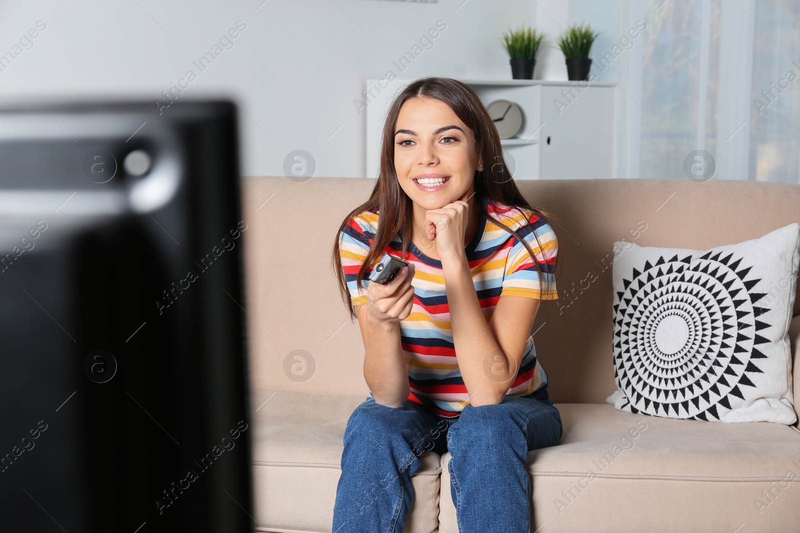 Photo of Beautiful young woman watching TV on sofa at home