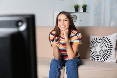 Photo of Beautiful young woman watching TV on sofa at home