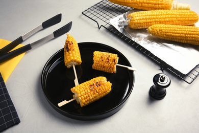 Ceramic plate with grilled corn cobs on light background