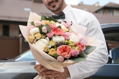 Young man with beautiful flower bouquet near car outdoors, closeup view