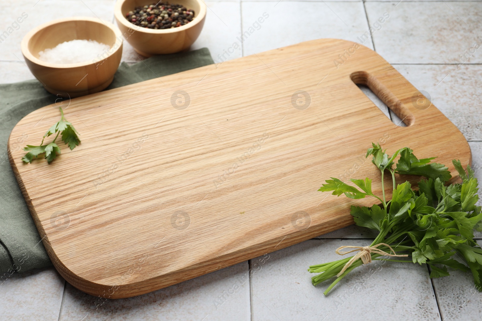 Photo of Cutting board, salt, pepper and parsley on white tiled table. Space for text