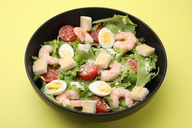 Delicious Caesar salad with shrimps on yellow table, closeup