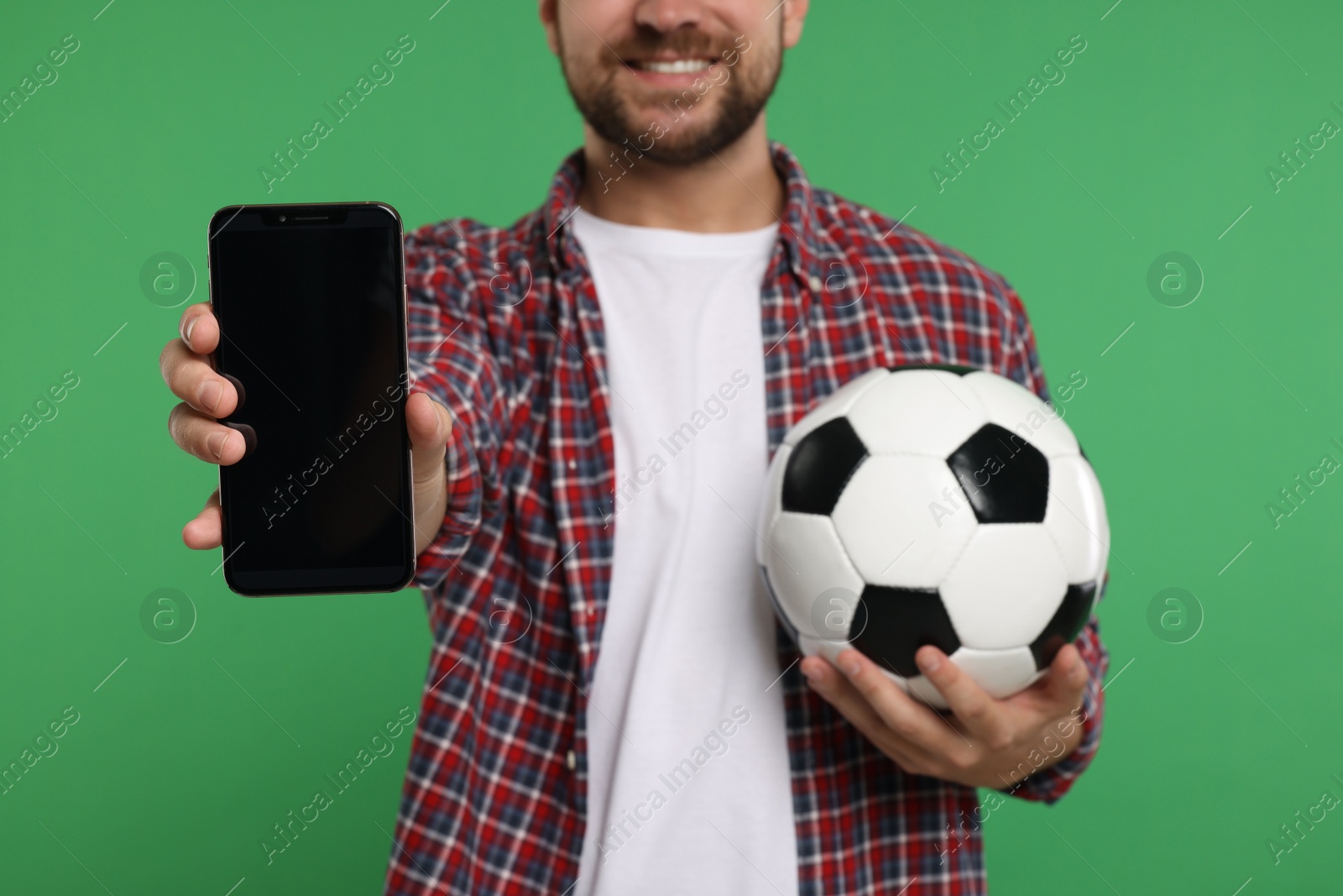 Photo of Sports fan with ball and smartphone on green background, closeup