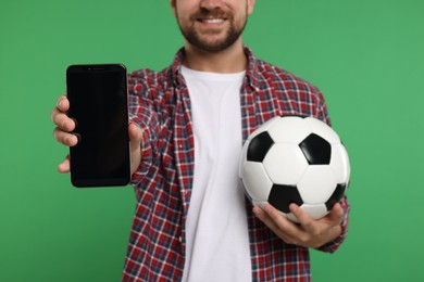 Sports fan with ball and smartphone on green background, closeup