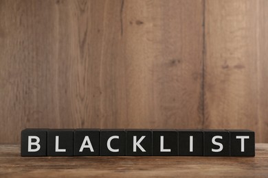 Photo of Black cubes with word Blacklist on wooden table