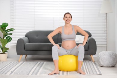 Pregnant woman sitting on fitness ball in room. Home yoga