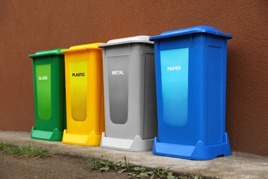 Many color recycling bins near brown wall outdoors