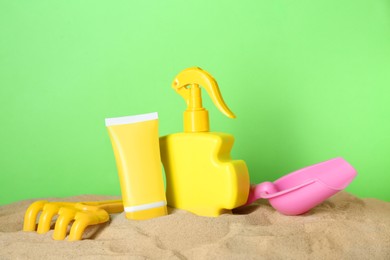 Suntan products and plastic beach toys on sand against green background