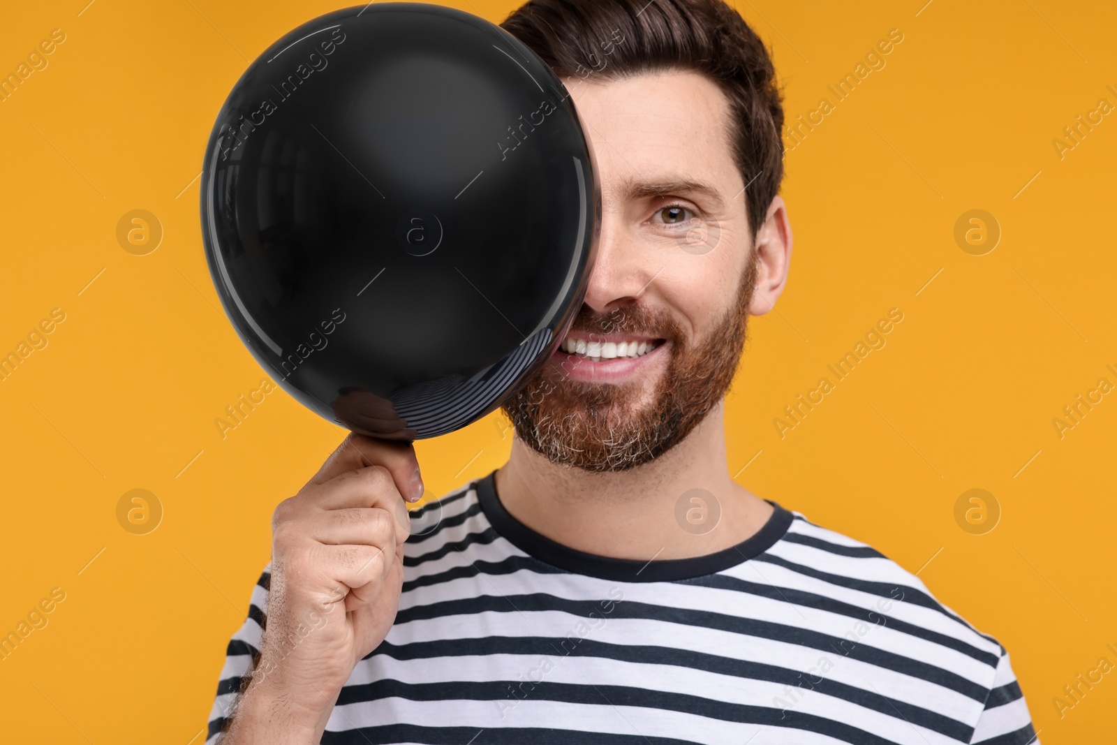 Photo of Happy man with black balloon on yellow background